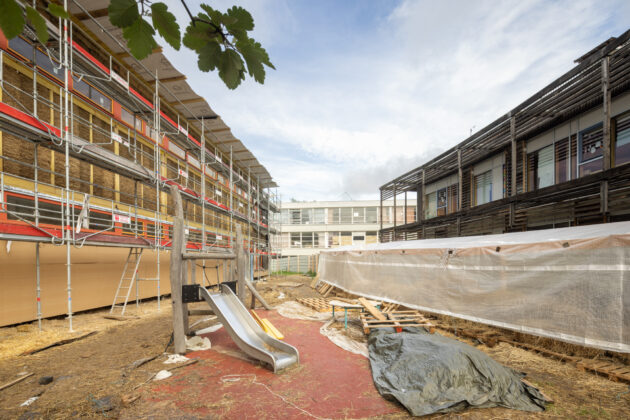 Le chantier de l'ITE paille face au centre de loisirs Jacques Chirac en paille porteuse. Au fond, l'école existante voisine construite sur le même modèle que celle en rénovation // Juan Sepulveda / Topophile