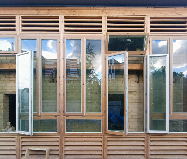 Le mur trombe en cours de finition : une lame d'air ventilé (ou non) entre des fenêtres de réemploi et un mur en brique de terre crue // Archipel zéro - Lao / Topophile
