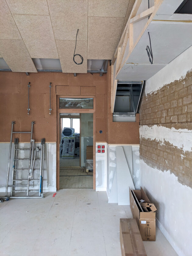 Place au second oeuvre dans la salle de classe : panneau acoutique au plafond, plaque de terre crue sur la partie haute des cloisons, enduit sur les blocs de terre comprimée... une gaine de ventilation naturelle en plaque de plâtre prend forme sur une ossature en bois. L'échangeur reste en alu // Martin Paquot / Topophile